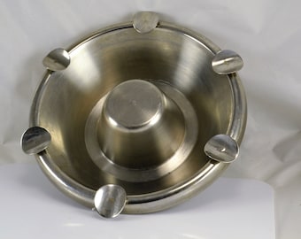 May include: A silver metal ashtray with four slots for cigarettes. The ashtray has a central bowl for collecting ash.
