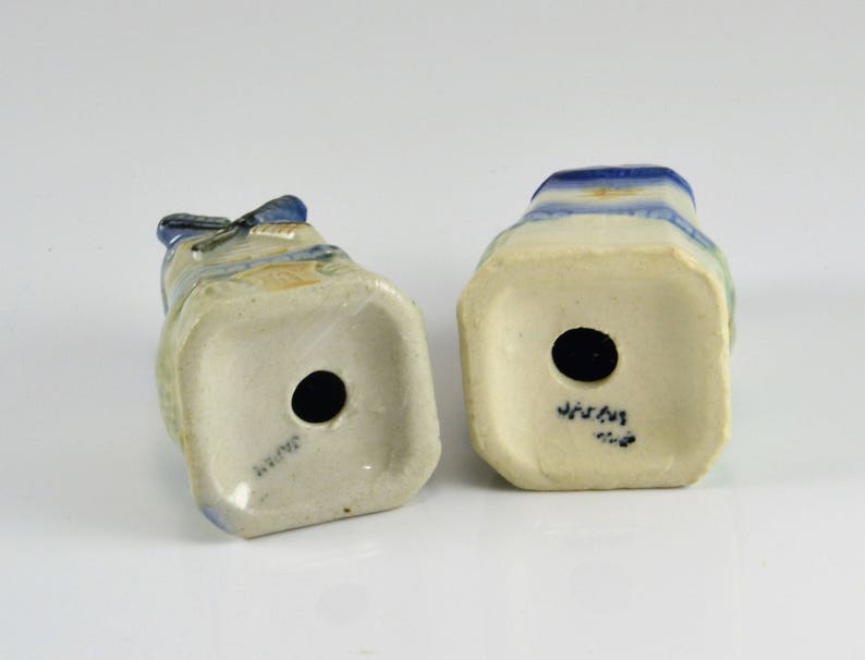 May include: Two ceramic salt and pepper shakers with a blue and white design. The shakers are shaped like people and have a hole in the bottom for filling. The bottom of the shakers are marked "JAPAN".