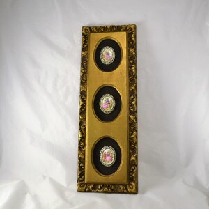 May include: A gold framed wall decor with three round porcelain medallions featuring images of people in vintage clothing.