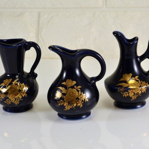 Peut inclure: Trois petits pichets en céramique bleue avec des motifs floraux dorés. Les pichets ont un corps rond et une anse incurvée.