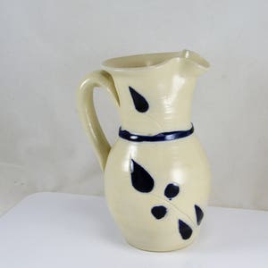 May include: A white ceramic pitcher with a blue and white leaf design. The pitcher has a wide mouth and a handle.