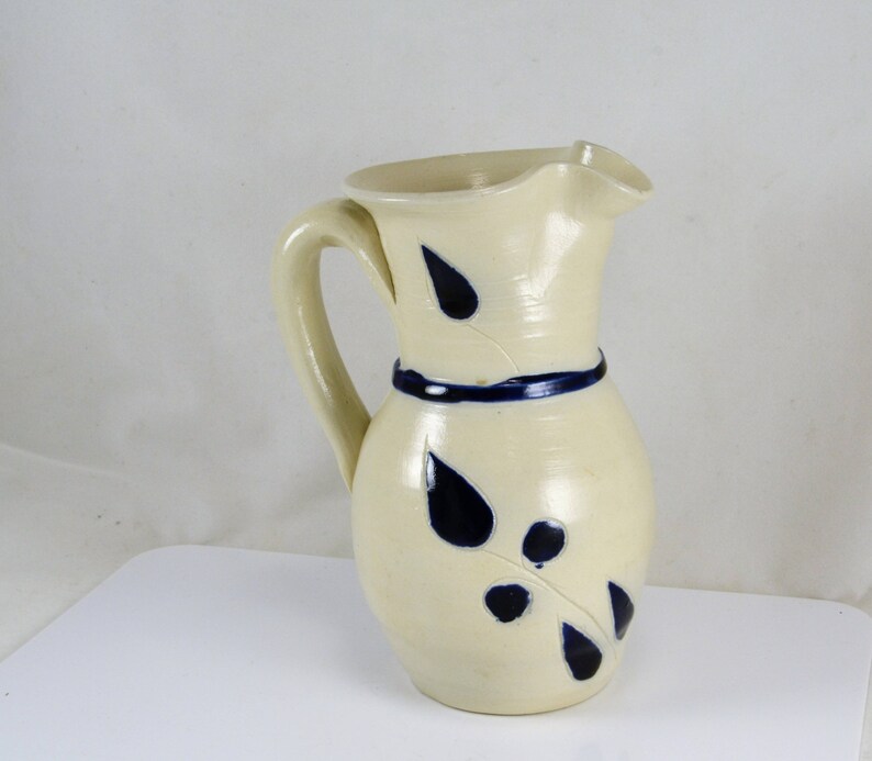 May include: A white ceramic pitcher with a blue and white leaf design. The pitcher has a wide mouth and a handle.
