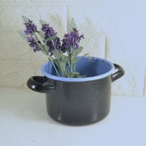 May include: A black enamel pot with a light blue rim, filled with purple and blue artificial lavender flowers.
