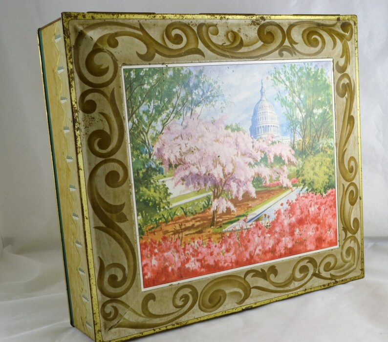 K&ouml;nnte beinhalten: Vintage Blechdose mit einem goldenen und wei&szlig;en verzierten Rahmen und einem farbenfrohen Bild des US-Kapitols mit Kirschbl&uuml;ten und Azaleen in voller Bl&uuml;te.