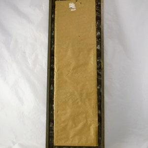 May include: A brown rectangular framed picture with a brown paper backing. The frame has a decorative, textured border.