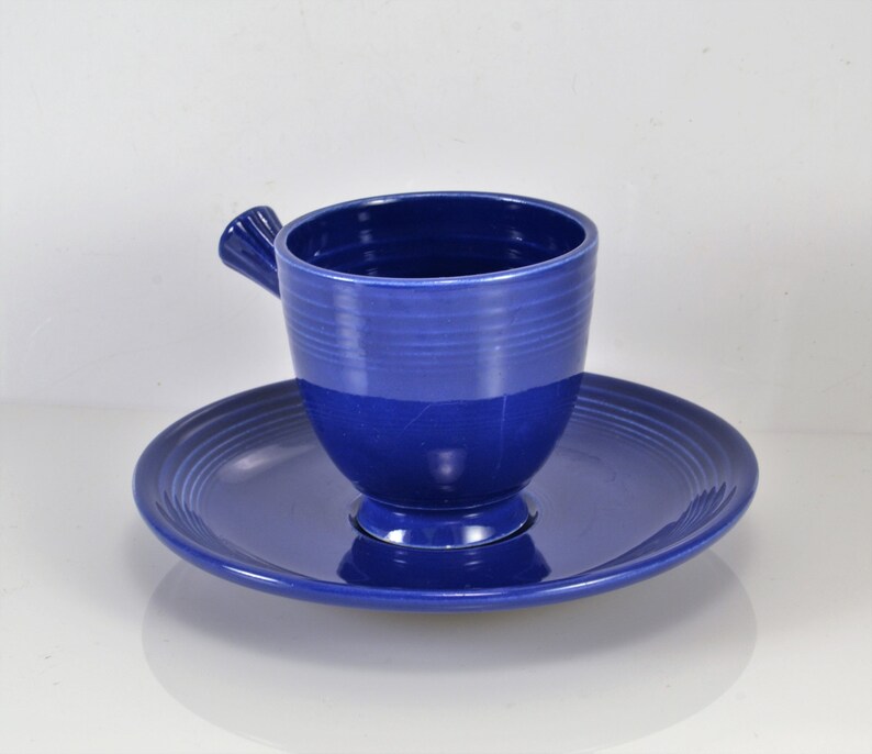 May include: A blue ceramic teacup and saucer set. The cup has a unique handle and the saucer has a ridged design.