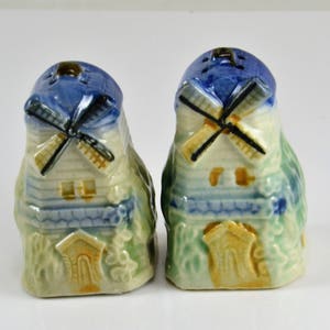 May include: A pair of ceramic salt and pepper shakers shaped like windmills. The shakers are painted in shades of blue, green, and yellow, with white accents. The windmills have white blades and are topped with blue roofs.