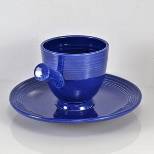 May include: A blue ceramic teacup and saucer set. The cup has a unique handle and the saucer has a scalloped edge.