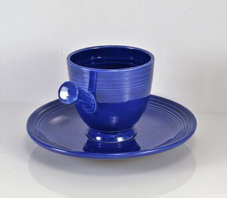 May include: A blue ceramic teacup and saucer set. The cup has a unique handle and the saucer has a scalloped edge.