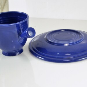 May include: A blue ceramic teacup and saucer set. The cup has a unique handle and a rounded shape. The saucer is a simple round shape.