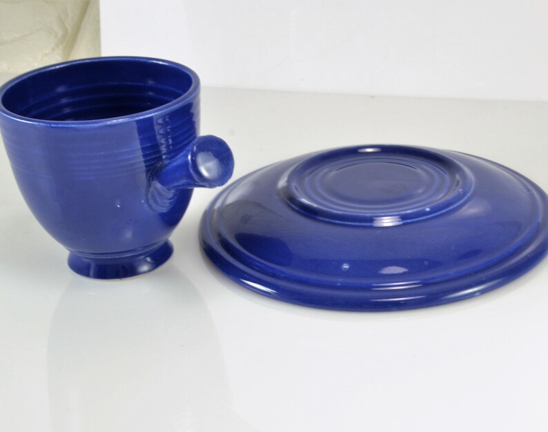 May include: A blue ceramic teacup and saucer set. The cup has a unique handle and a rounded shape. The saucer is a simple round shape.