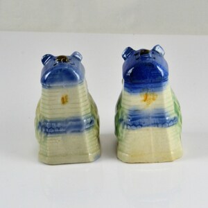 May include: A pair of vintage salt and pepper shakers shaped like houses. The shakers are made of ceramic and are painted in shades of blue, green, and white. The roofs of the houses are blue and have a white trim. The sides of the houses are white with blue and green stripes. The shakers are in good condition with no chips or cracks.