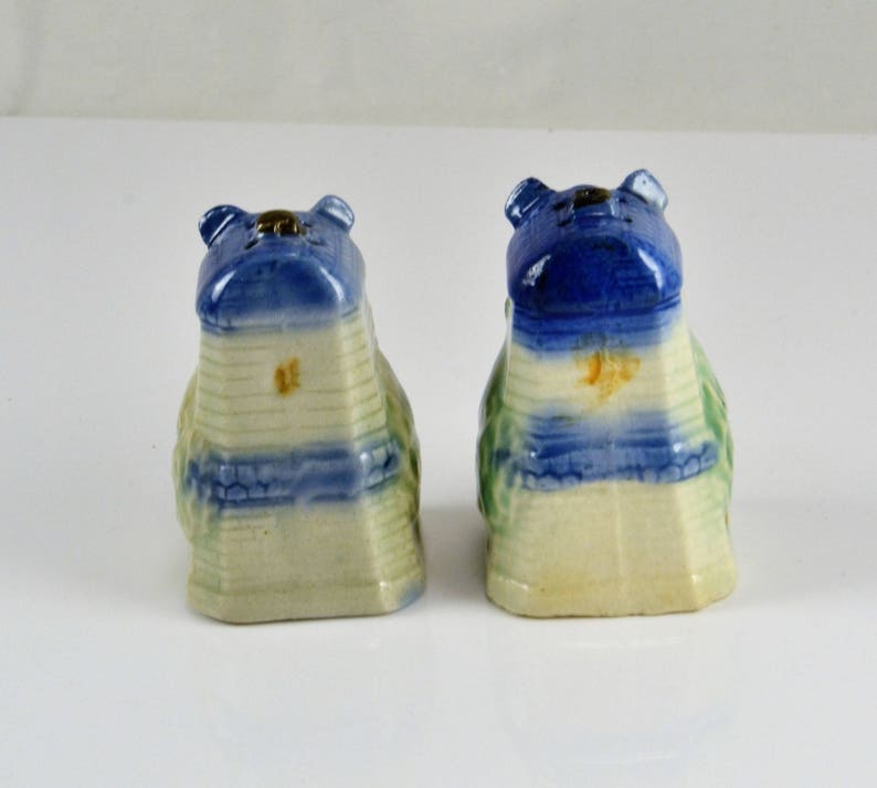 May include: A pair of vintage salt and pepper shakers shaped like houses. The shakers are made of ceramic and are painted in shades of blue, green, and white. The roofs of the houses are blue and have a white trim. The sides of the houses are white with blue and green stripes. The shakers are in good condition with no chips or cracks.