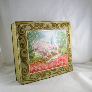 K&ouml;nnte beinhalten: Vintage Blechdose mit einem verzierten goldenen und wei&szlig;en Rahmen und einem farbenfrohen Bild des US-Kapitols mit Kirschbl&uuml;ten im Vordergrund.