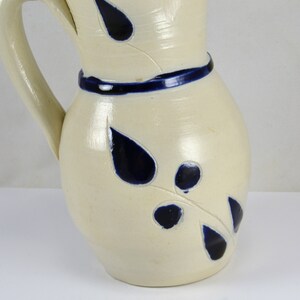 May include: A white ceramic pitcher with a blue rim and blue leaf designs. The pitcher has a handle and a rounded body.