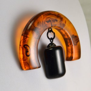 Peut inclure: Une broche vintage avec une grande pièce en résine de couleur ambre semi-circulaire et un pendentif en résine rectangulaire noir suspendu à une chaîne métallique.