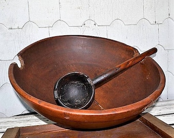 May include: A large, wooden bowl with a dark brown finish and a wooden ladle inside. The bowl has a unique shape with a wide rim and a slightly curved bottom. The ladle is also made of wood and has a dark brown finish.
