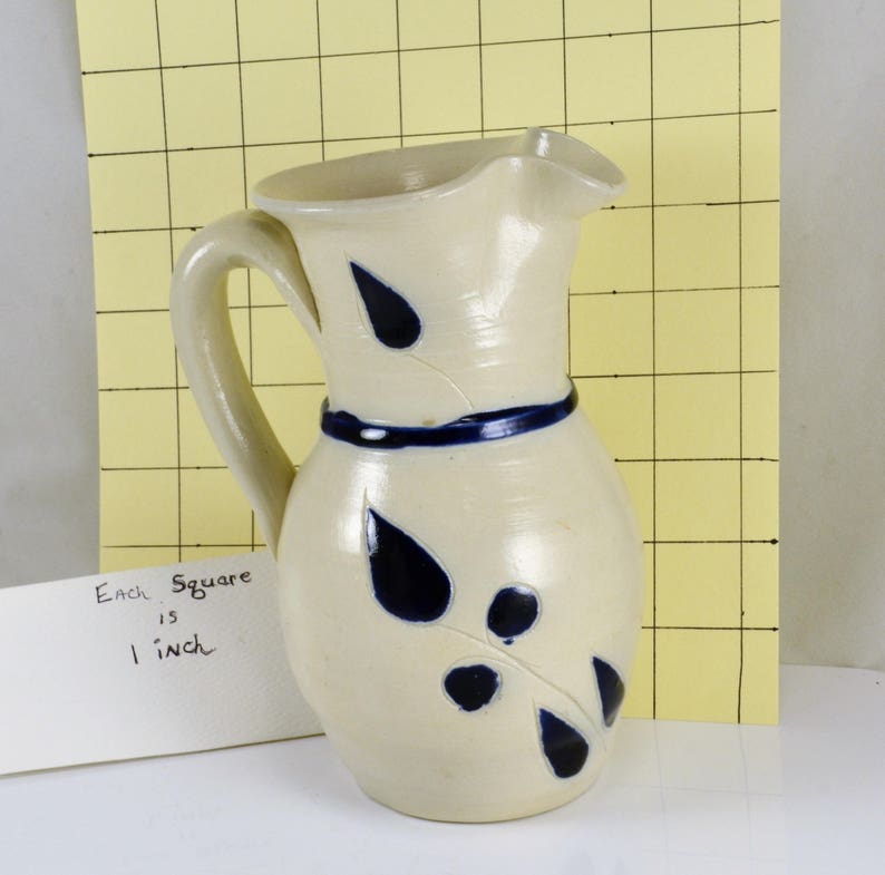 May include: A white ceramic pitcher with a blue glaze and a leaf design. Each square is 1 inch.