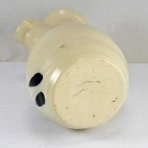 May include: A white ceramic pitcher with blue leaf designs. The pitcher has a rounded body and a wide mouth. The bottom of the pitcher is unglazed and shows signs of wear.