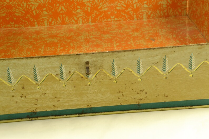 K&ouml;nnte beinhalten: Eine vintage Metalldose mit einem dekorativen gr&uuml;nen, gelben und wei&szlig;en Rand. Das Innere der Dose ist mit orangefarbenem Musterpapier ausgekleidet.