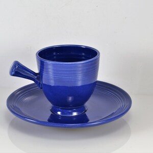 May include: A blue ceramic teacup and saucer set. The cup has a handle and a rounded shape. The saucer has a scalloped edge.