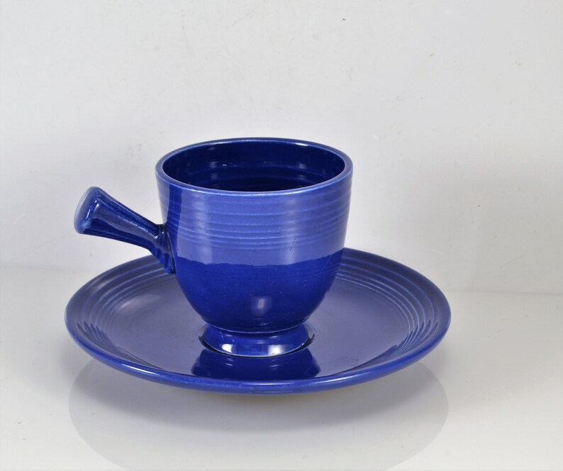May include: A blue ceramic teacup and saucer set. The cup has a handle and a rounded shape. The saucer has a scalloped edge.