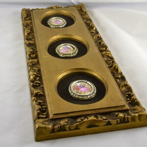 May include: A gold-colored frame with three circular openings, each containing a small framed image of a couple in a romantic setting. The frame has an ornate design with intricate details.