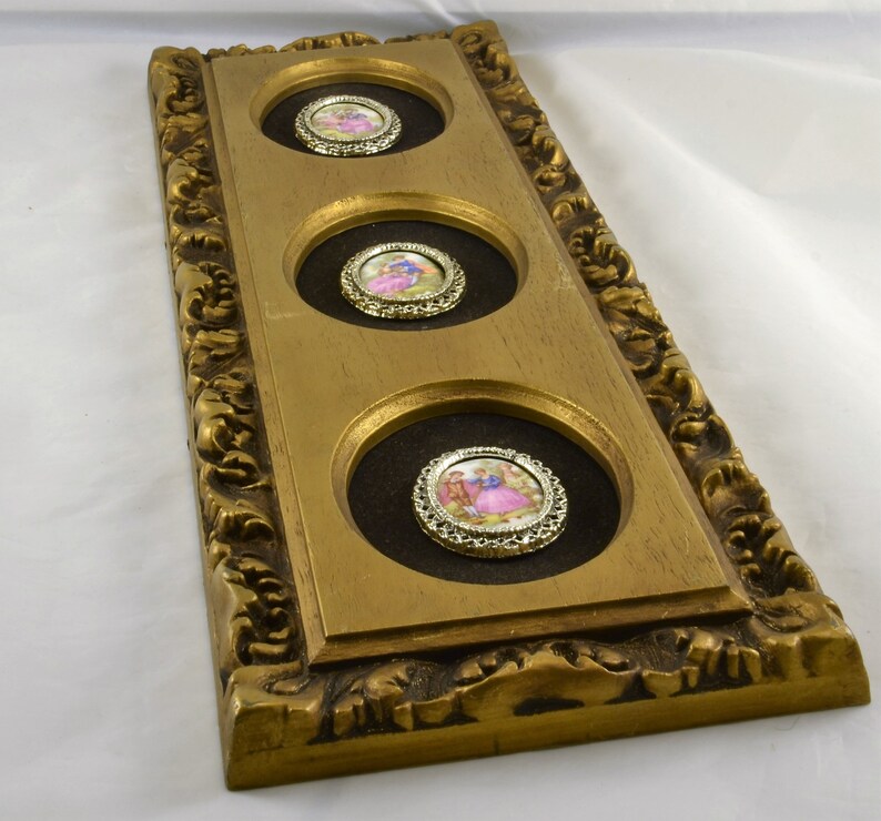 May include: A gold-colored frame with three circular openings, each containing a small framed image of a couple in a romantic setting. The frame has an ornate design with intricate details.