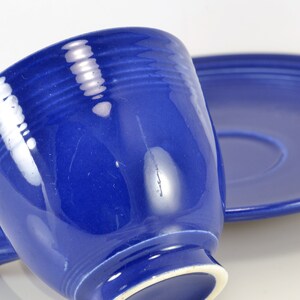 May include: A blue ceramic teacup and saucer set. The cup has a rounded shape and a handle. The saucer is round and has a slightly raised edge.