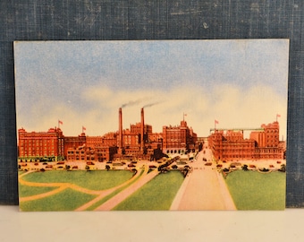 Peut inclure: Une carte postale vintage représentant un grand bâtiment en briques avec plusieurs cheminées. Le bâtiment est entouré d'une zone herbeuse et d'une route avec des voitures. La carte postale est en bon état avec quelques signes d'usure.