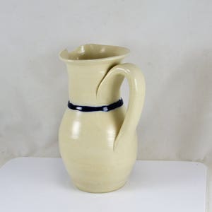 May include: A cream-colored ceramic pitcher with a blue stripe around the middle and a curved handle.
