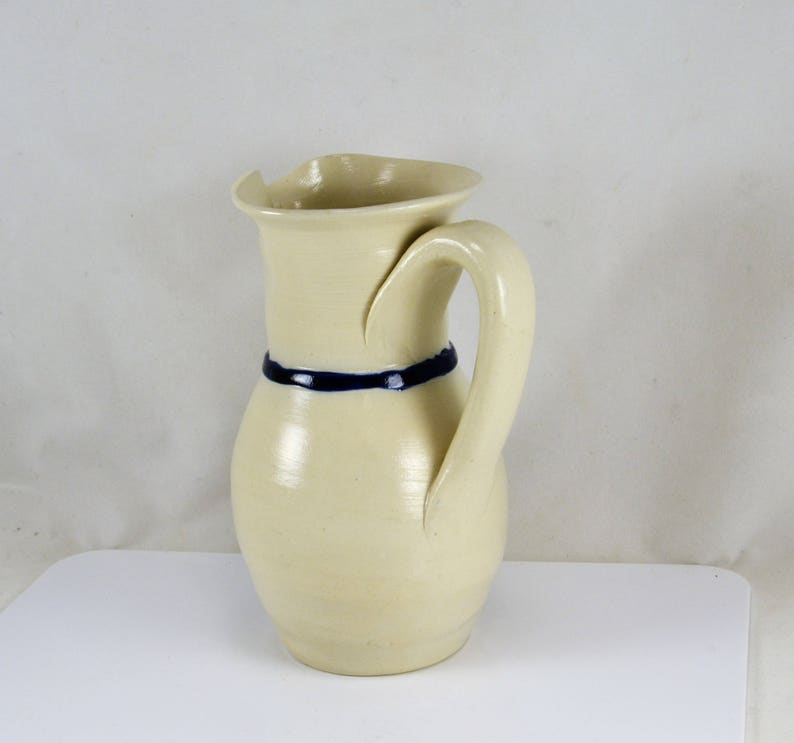 May include: A cream-colored ceramic pitcher with a blue stripe around the middle and a curved handle.
