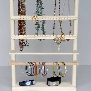 May include: A wooden jewellery stand with three tiers for necklaces and earrings, and a bottom rod for bracelets and watches. The stand is made of natural wood and has a light brown finish.