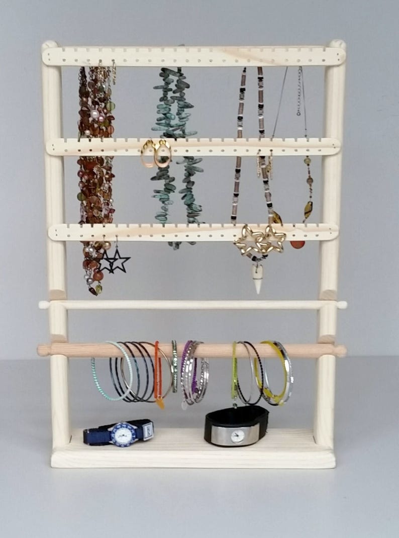 May include: A wooden jewellery stand with three tiers for necklaces and earrings, and a bottom rod for bracelets and watches. The stand is made of natural wood and has a light brown finish.