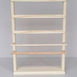 May include: A wooden earring stand with four shelves and a rolling bar. The stand is made of natural wood and has a light brown finish.