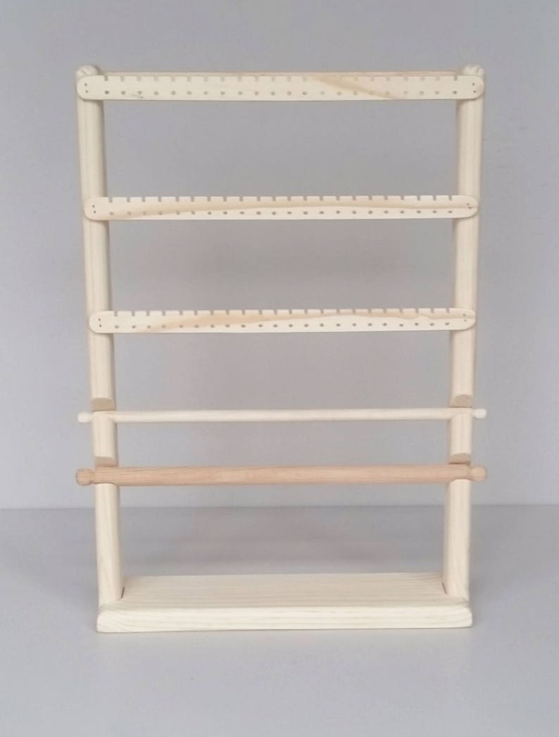 May include: A wooden earring stand with four shelves and a rolling bar. The stand is made of natural wood and has a light brown finish.