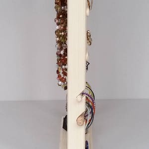 May include: A wooden jewellery stand with a vertical section for necklaces and a horizontal section for bracelets. The stand is made of natural wood and has a simple design.