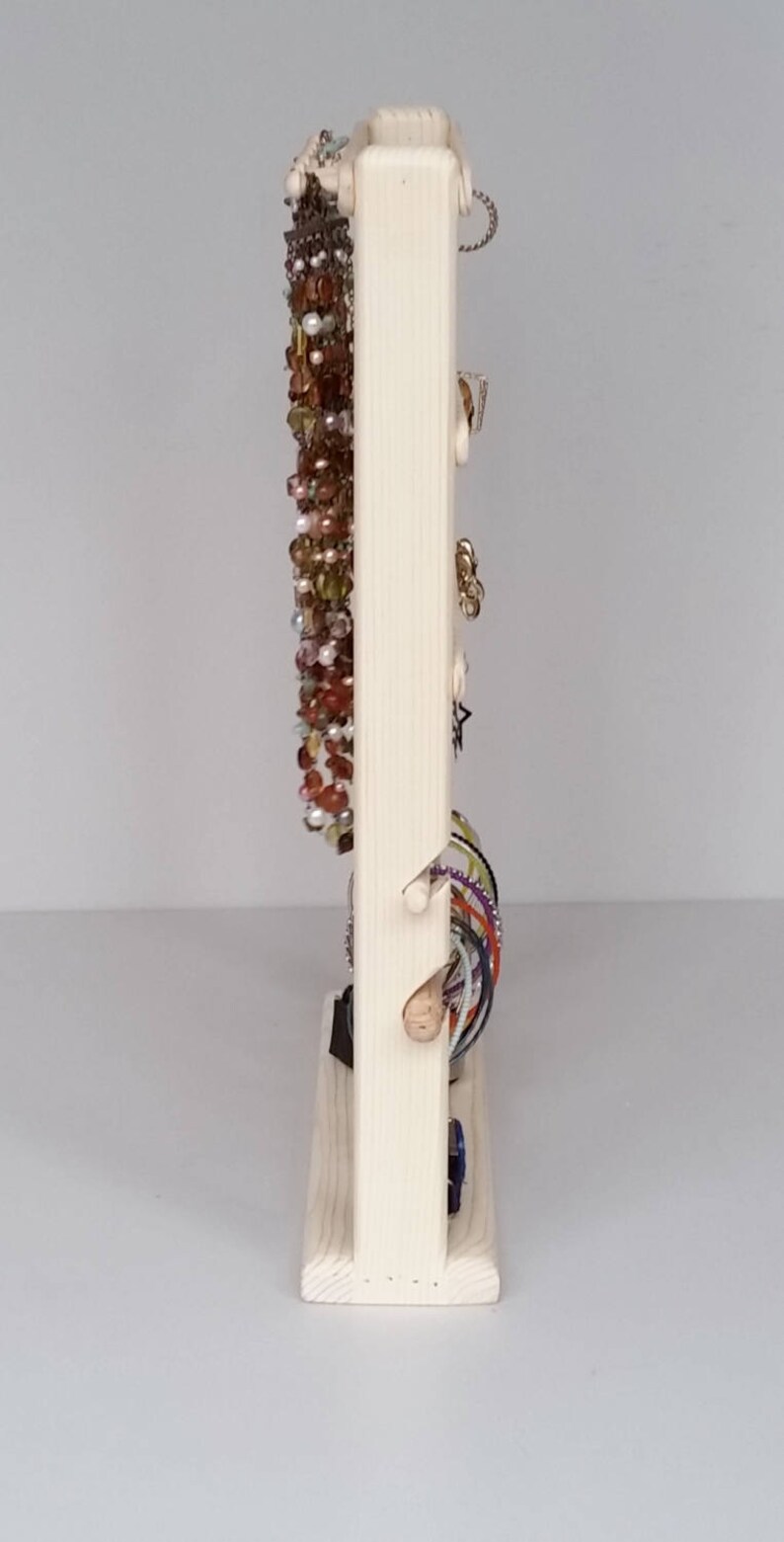 May include: A wooden jewellery stand with a vertical section for necklaces and a horizontal section for bracelets. The stand is made of natural wood and has a simple design.