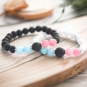 May include: Two beaded bracelets, one black with blue and white beads, the other white with pink and blue beads.