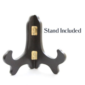 May include: A black wooden display stand with a gold hinge. The stand is designed to hold a plate or other flat object. "Stand Included" is written in black text on a white background.