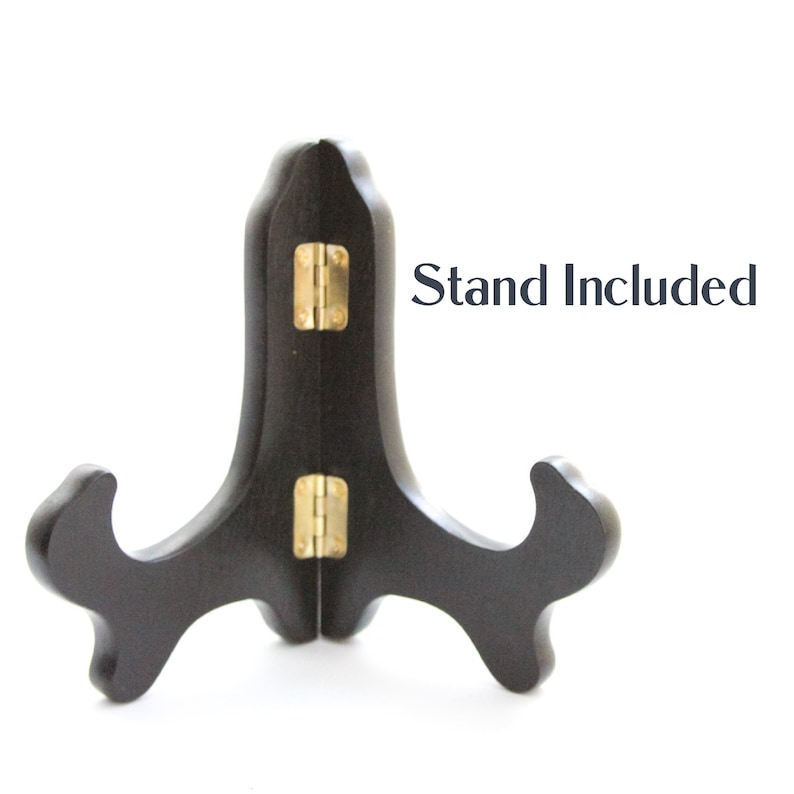 May include: A black wooden display stand with a gold hinge. The stand is designed to hold a plate or other flat object. "Stand Included" is written in black text on a white background.