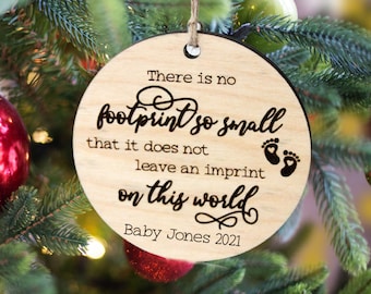 May include: A round wooden ornament with the text "There is no footprint so small that it does not leave an imprint on this world" and the text "Baby Jones 2021".
