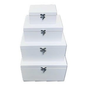 May include: Four white wooden boxes with hinged lids and silver clasps, stacked in decreasing size. The boxes are all plain and unadorned.