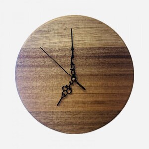 May include: Circular wooden wall clock with a natural wood grain. The clock has black hands and a decorative black centre design. The hands indicate approximately 7 o'clock.