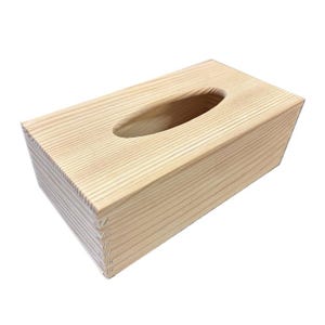 May include: A rectangular wooden tissue box in a natural finish. It features an oval opening on top for dispensing tissues. The wood grain is visible, providing texture. The box is designed to hold standard tissue boxes. Dimensions are approximately 25 cm long.