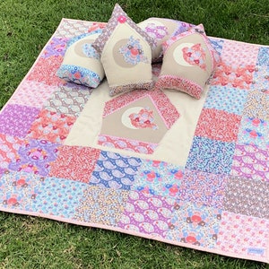 May include: A patchwork quilt with a pink, purple, and blue floral pattern. The quilt has a white border and is decorated with three pillows featuring a bird design.