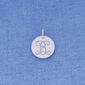 May include: A silver round pendant with a cursive letter "B" engraved on it.