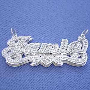 May include: Silver nameplate necklace with the name "Jamie" spelled out in a cursive font with a small heart charm. The nameplate has a diamond-like pattern.