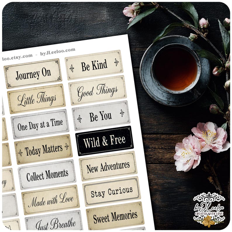 May include: A sheet of vintage-style stickers with inspirational phrases like "Journey On," "Be Kind," and "Wild & Free." The stickers have a cream and black color scheme with decorative borders. A cup of tea and flowers are in the background.