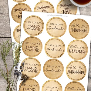 K&ouml;nnte beinhalten: Zw&ouml;lf runde, bedruckbare Papieretiketten mit einem Vintage-Look im Used-Look. Die Etiketten zeigen verschiedene S&auml;tze zu handgefertigten Waren, wie "Handgefertigt mit Liebe" und "Hallo, ich bin handgefertigt".